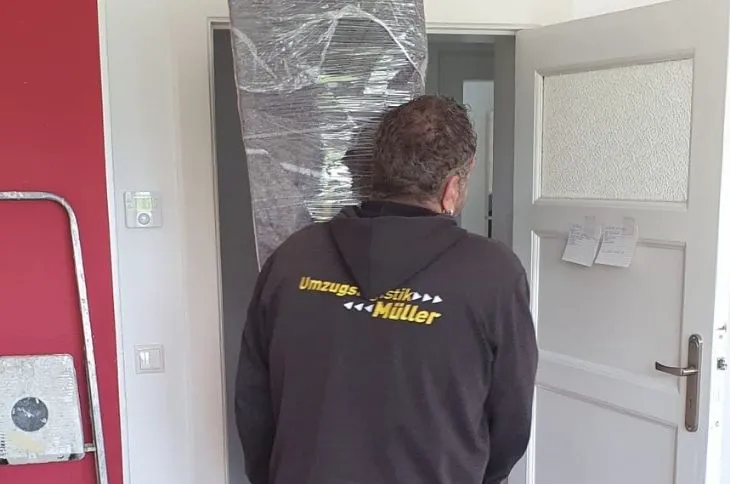 umzugshelfer traegt hohes verpacktes moebel durch wohnung