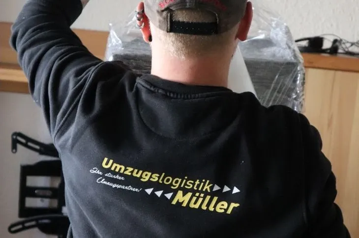 umzugshelfer traegt moebelstueck mit schutzfolie in innenraum